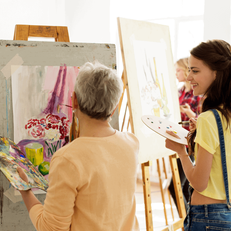 People painting on canvases in an art class, focusing on floral still lifes using palettes and brushes.